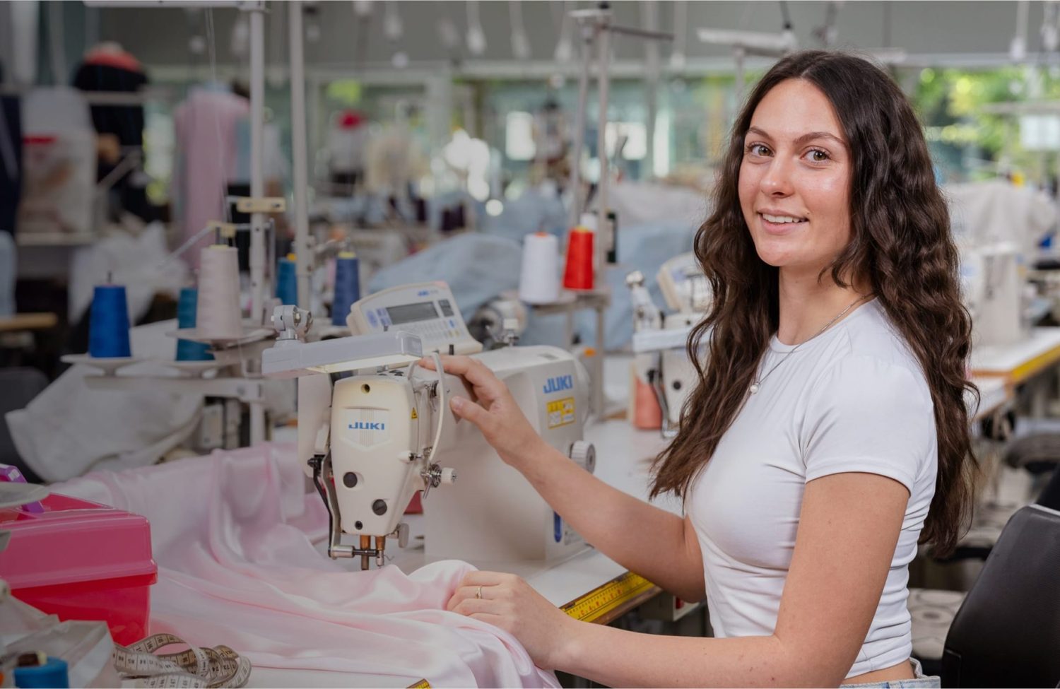 A young woman smiles at the camera while working at a sewing machine.