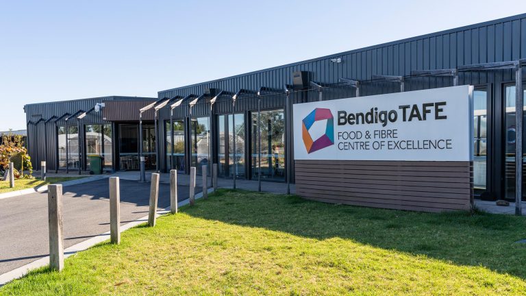 Exterior sign and entrance area of the Bendigo TAFE Food & Fibre Centre of Excellence, showing the low-slung, dark-colored building with large windows and a grassy area in the foreground.