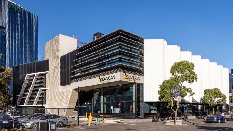 Street-level view of the modern, architecturally distinct Kangan Institute Docklands campus building, featuring a multi-faceted facade with glass and white and black panels
