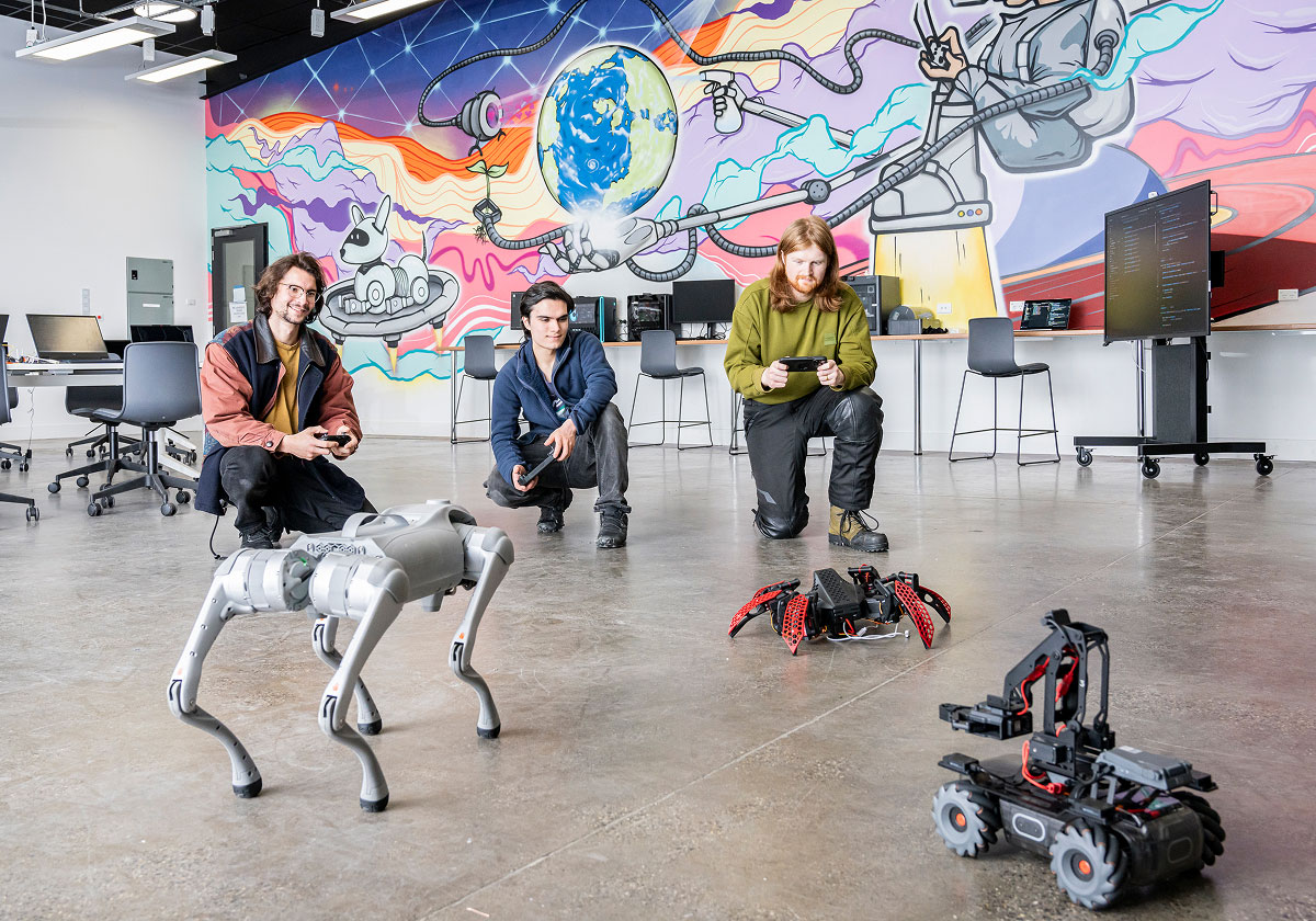 Interior of a brightly lit digital workshop space, featuring a colorful mural on the wall, and students or instructors interacting with a small robotic dog.