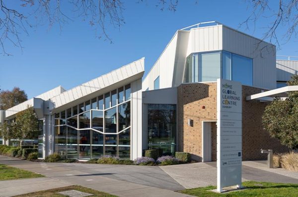 Exterior view of the Hume Global Learning Centre in Sunbury, a building with contemporary, angular architecture and large glass windows, featuring a sign post detailing the services offered.