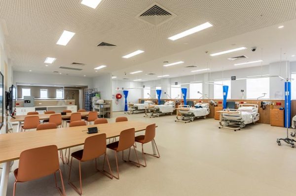 Spacious interior of a training facility, featuring a simulation ward with several hospital beds and a large, adjacent classroom area with long tables and chairs.