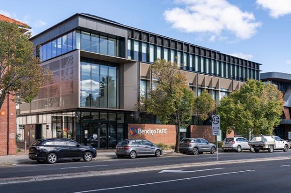Modern, three-story building for Bendigo TAFE City campus with large windows, facing a street with parked cars.