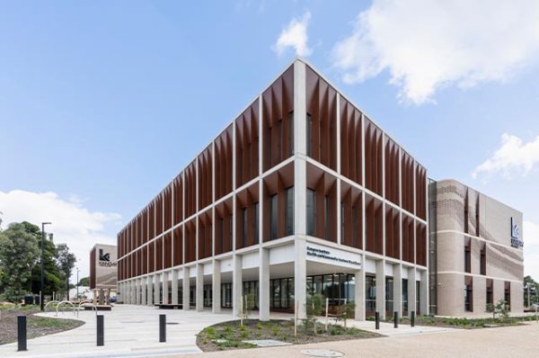 Exterior view of the Kangan Institute Health and Community Centre of Excellence (HaCCoE) building at Broadmeadows, featuring multiple floors with vertical wooden or brown slats covering the windows.