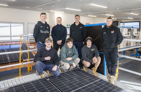 Seven people, including teacher Matt Roberts and students, in the Bendigo TAFE clean energy lab surrounded by solar panels and inverters.
