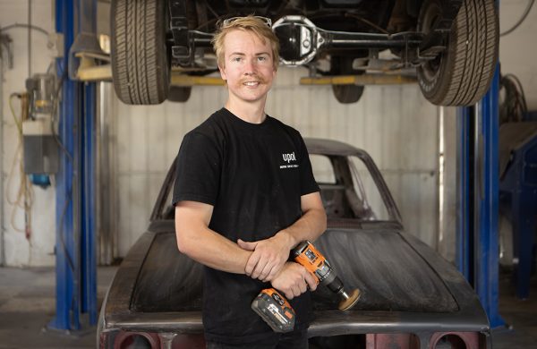 Student Wyatt Tucker holding hand tool in front of a car