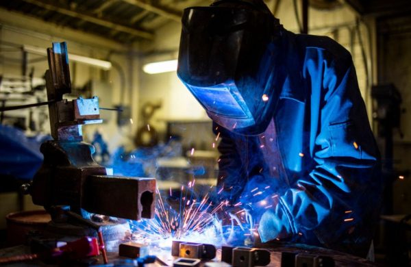 A person welding some metal with a welding mark over their face.
